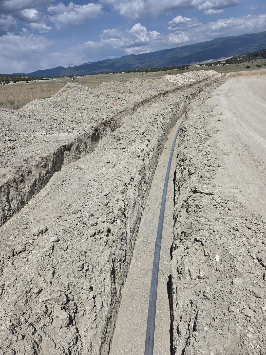 Long underground conduit run in an open trench alongside a dirt road, rural Utah