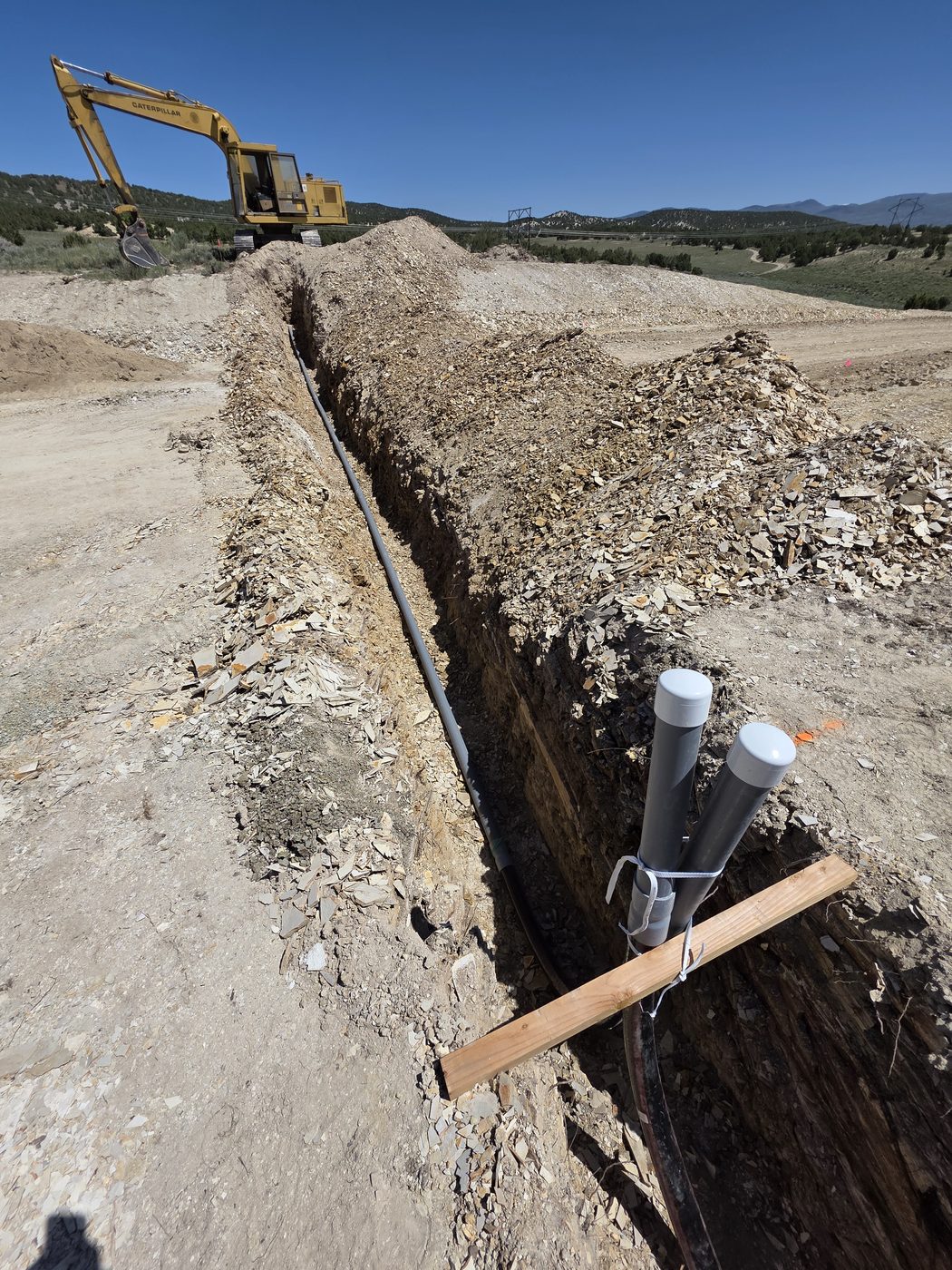 Conduit trench with a Caterpillar excavator and transmission lines in the distance, rural Utah