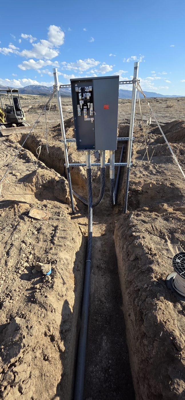 Open electrical service panel showing lugs with conductors running down into the trench below