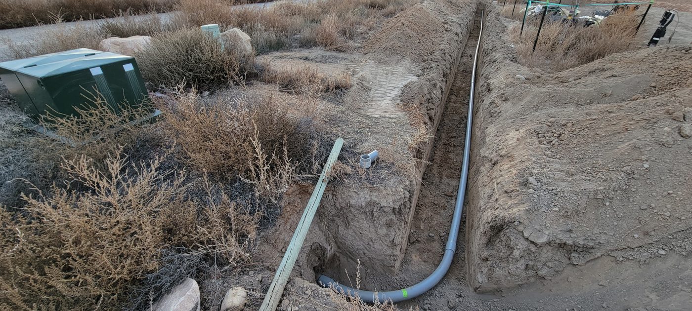 Conduit trench running to a green pad-mounted utility transformer on rural sagebrush ground