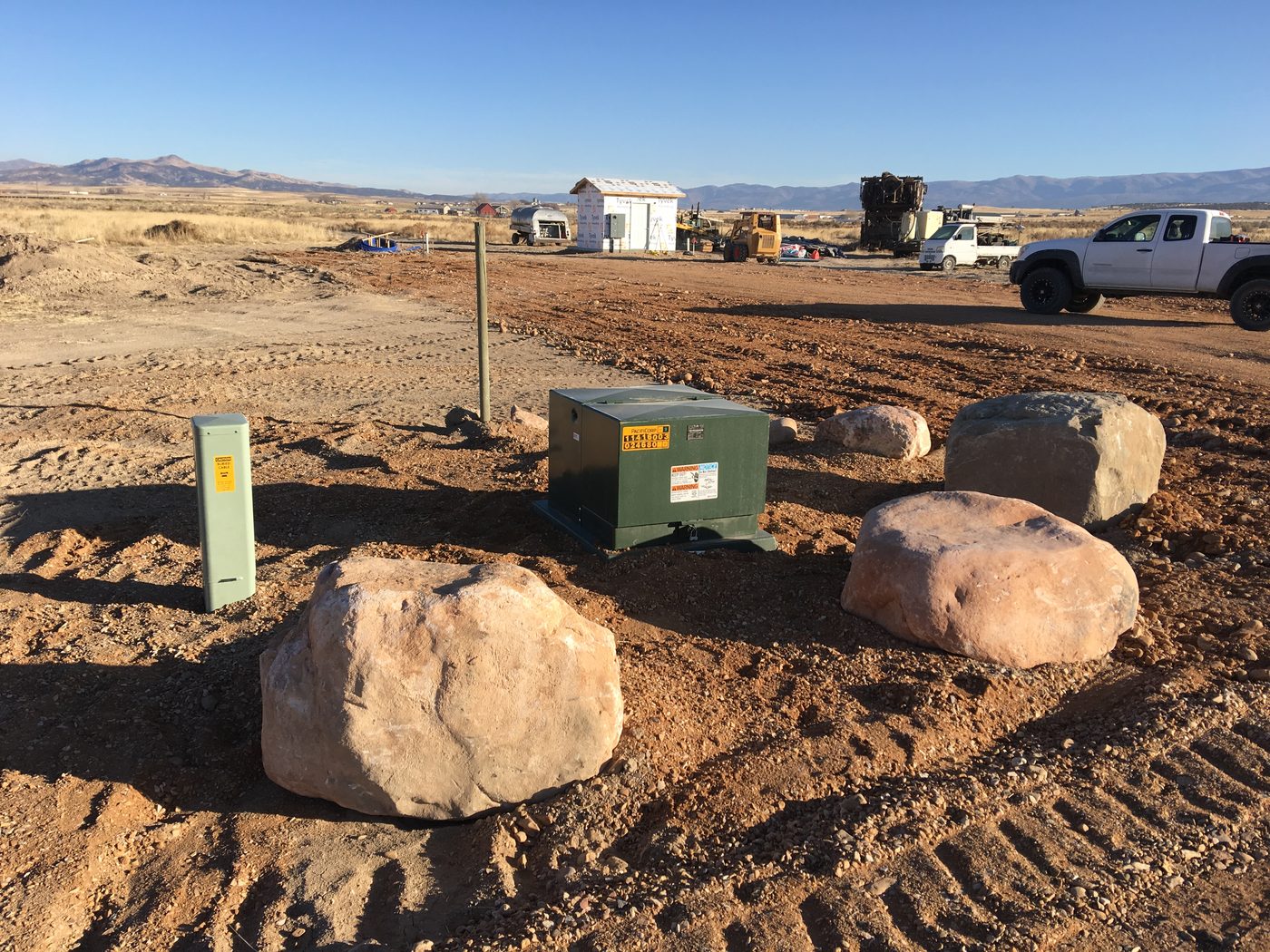 Pad-mounted utility transformer set and ringed with boulders for protection, with a buried cable marker beside it, rural Utah