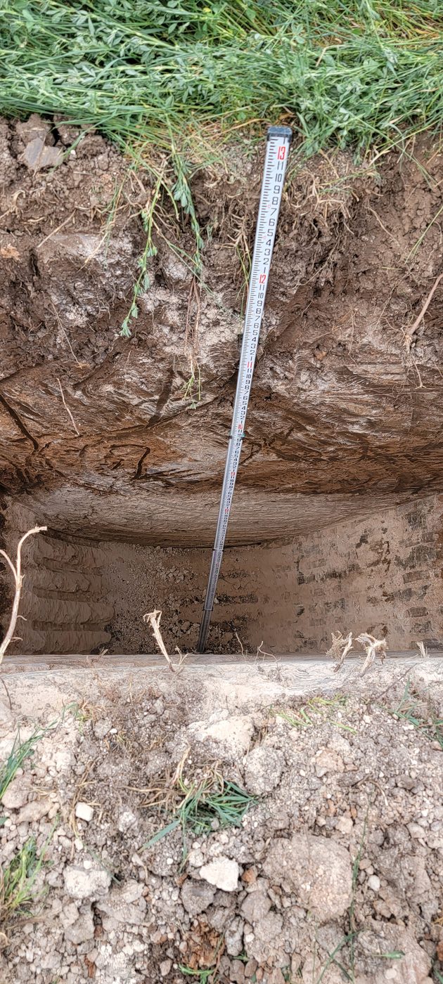 Soil evaluation pit with a survey rod showing depth against clearly visible soil horizons, rural Utah