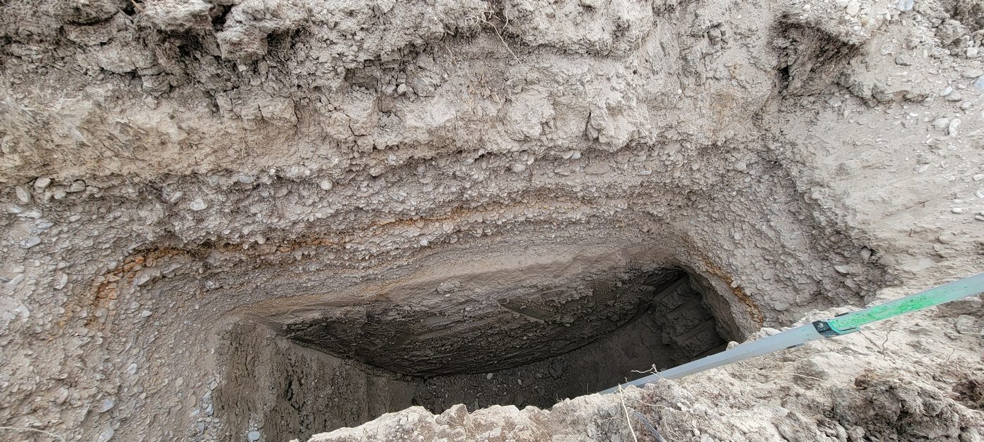 Close view of a soil pit wall showing stratified layers of cobble, sand and oxidized bands