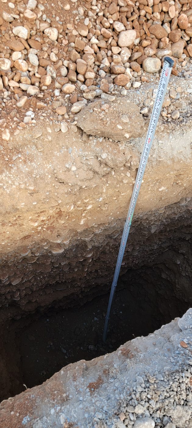 Soil evaluation pit with a survey rod showing a cobble-heavy soil profile, rural Utah