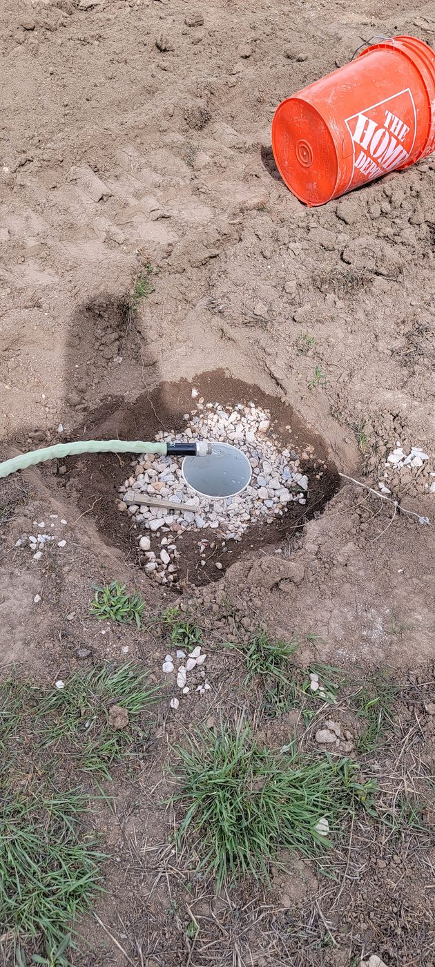 Percolation test hole with gravel base being pre-soaked from a hose during a perc test in Utah