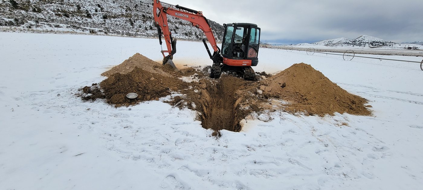 Kubota excavator digging a soil evaluation pit through frozen snow-covered ground in rural Utah