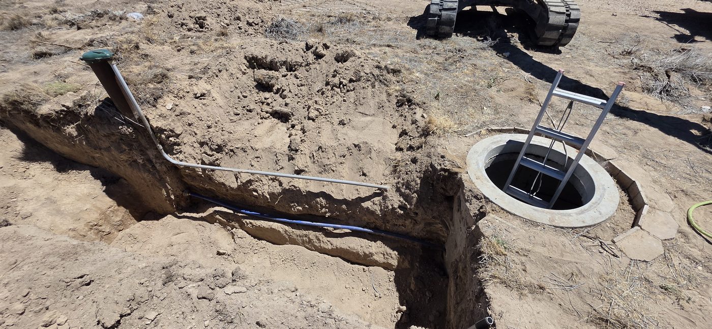 Concrete water vault with access ladder beside a trench carrying water line and conduit, rural Utah